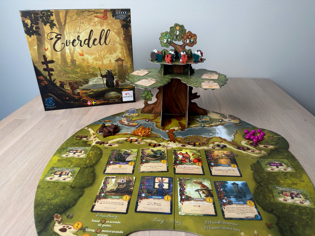 Everdell uppställt på ett bord: asken, det tredimensionella trädet och spelplanen med utlagda kort.