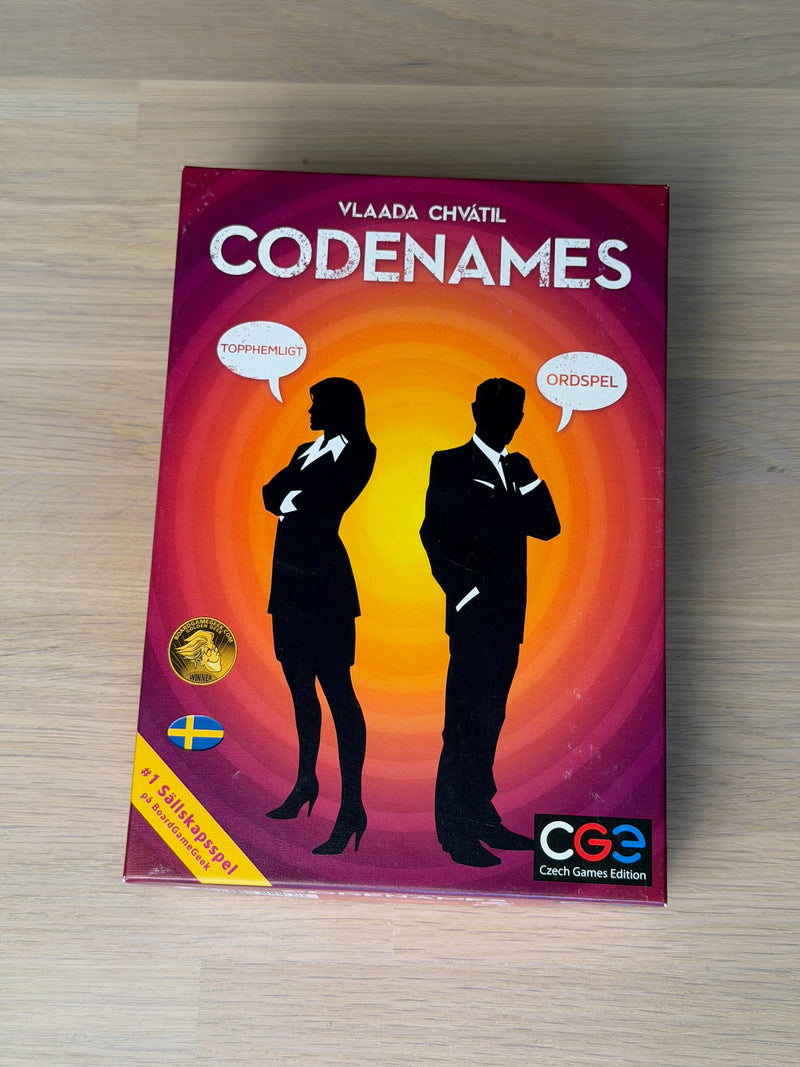 Codenames svenska ask fotograferad rakt uppifrån på ett ekgolv.
