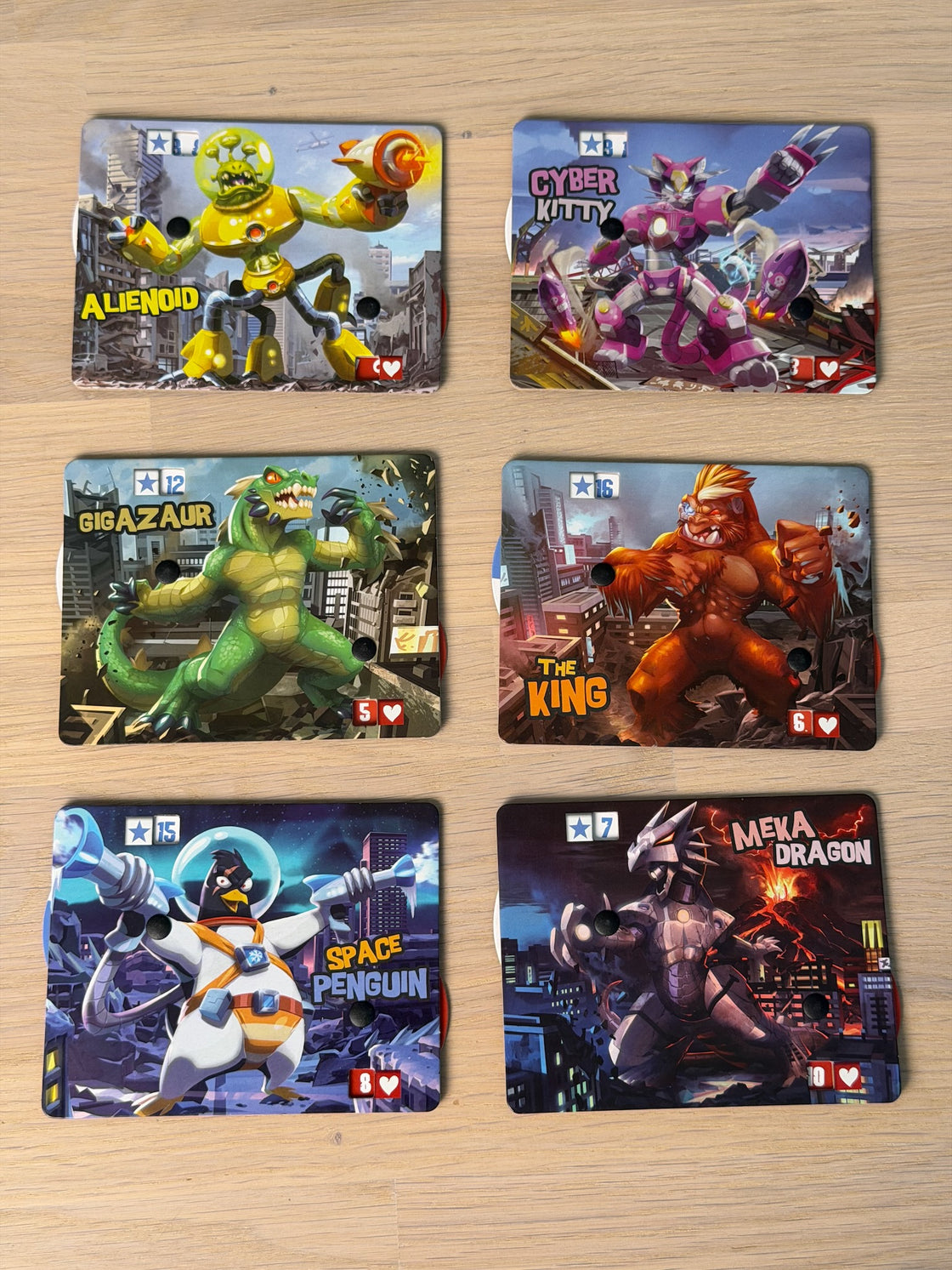 King of Tokyos sex monsterbräden utlagda i två rader på ett ekgolv: Alienoid, Cyber Kitty, Gigazaur, The King, Space Penguin och Meka Dragon.