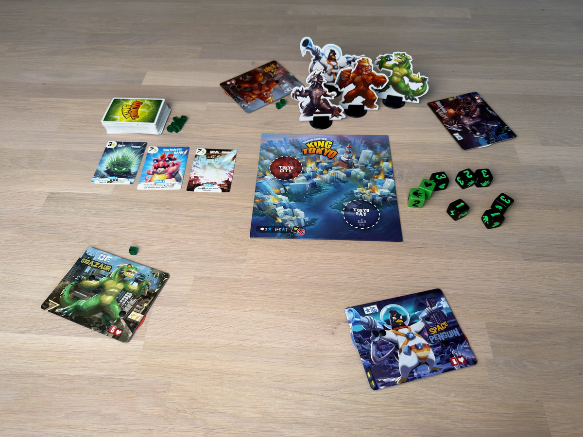 King of Tokyo uppdukat på ett ekgolv sett uppifrån: spelplan, monsterbräden, tärningar och kortlek.